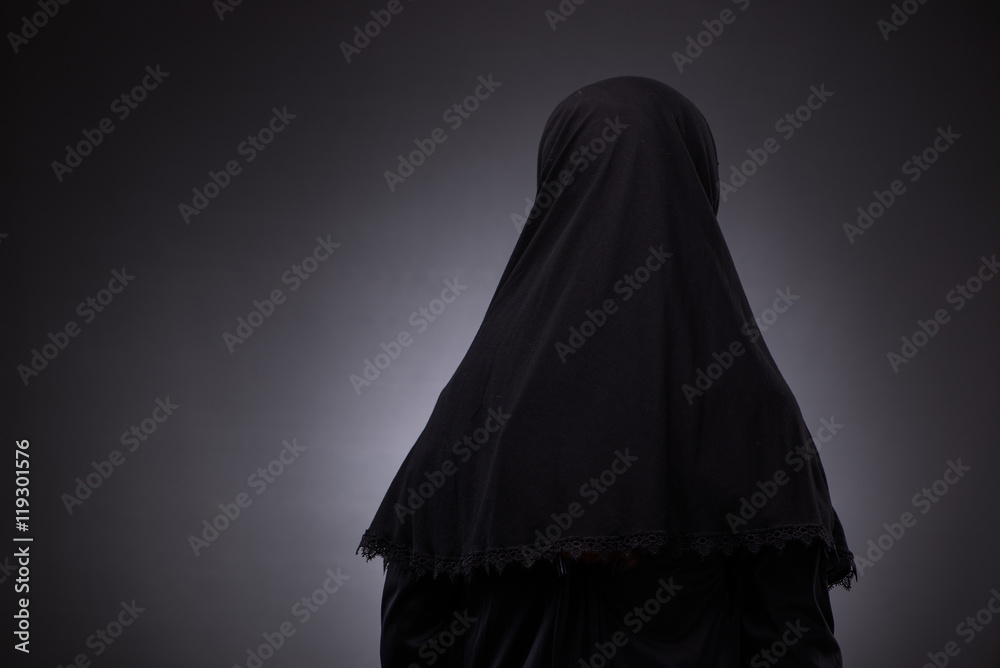 Muslim woman in black dress against dark background Muslim woman in black dress against dark background