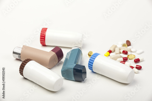 Various types of asthma inhalers and some pills on white