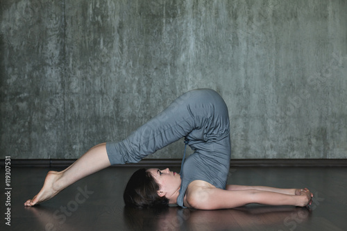Young woman practicing yoga on a background of gray concrete wall. Urban background. Monochrome image.
