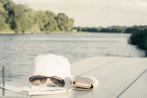 vacation and technology accessories on lakeside smartphone,  hat
