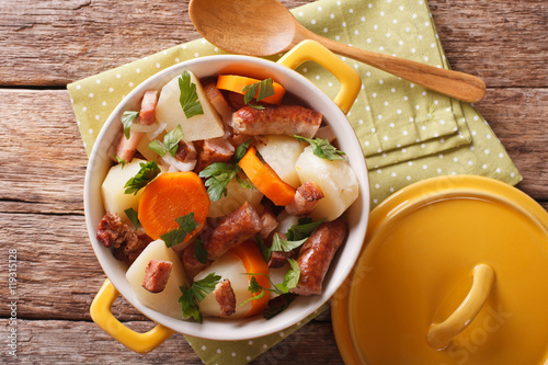 tasty Irish coddle with pork sausages, bacon and vegetables in a yellow pot. horizontal top view
