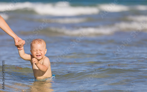 Adorable toddler boy enjoying swimming in the ocean on a sunny day. Mother and child in the sea. Family on vacations. Little baby in water, outdoors.