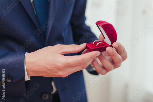 Hands of groom getting ready in suit. He holds the box with the wedding rings.