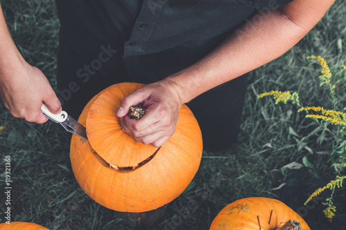 A close up of man's hand cuts a lid from a pumpkin as he prepares a jack-o-lantern. Halloween. Decoration for party.