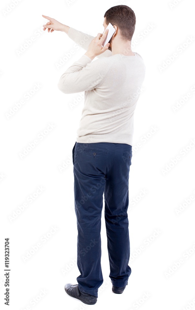 Back view of pointing young men talking on cell phone. bearded man in a white sweater warm white talking on smartphone and gives an indication of the hand. Back view of pointing young men talking on cell phone. bearded man in a white sweater warm white talking on smartphone and gives an indication of the hand.