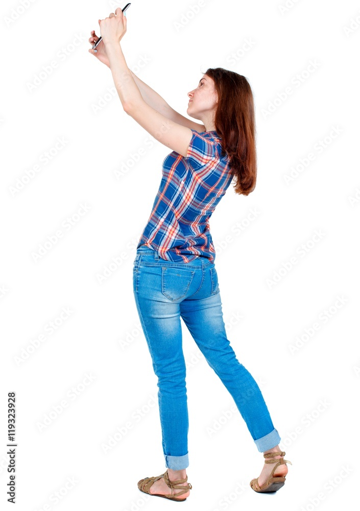 back view of standing young beautiful woman using a mobile phone. girl watching. Girl in plaid shirt standing sideways and photographs on your smartphone.