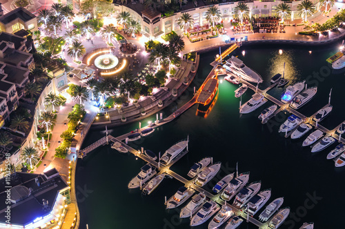 Amazing colorful dubai marina fountain and yacht dock during night. Beautiful sidewalk among tallest skyscrapers of the world. Dubai marina, United Arab Emirates. © marekkijevsky