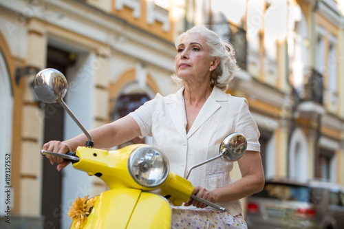 Woman holds scooter's steering wheel. Mature lady with confident face. I choose the right route. No obstacles during the trip.