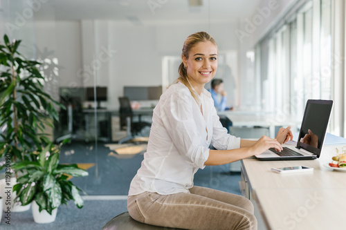 Business woman working on laptop in office while sitting on pilates ball