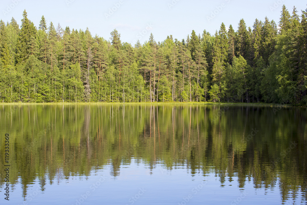 Obraz premium Silent evening by the lake. The sun is about to go down in Finland during late summer evening. The water is reflecting nicely the forest in the background.