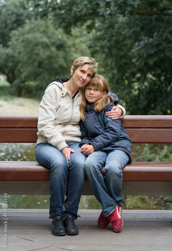 happy mother and daughter sitting embraced on bench happy mother and daughter sitting embraced on bench