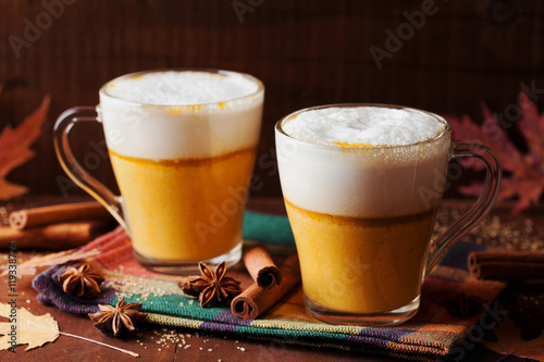 Pumpkin spiced latte or coffee in a glass on a wooden rustic table. Autumn or winter hot drink.