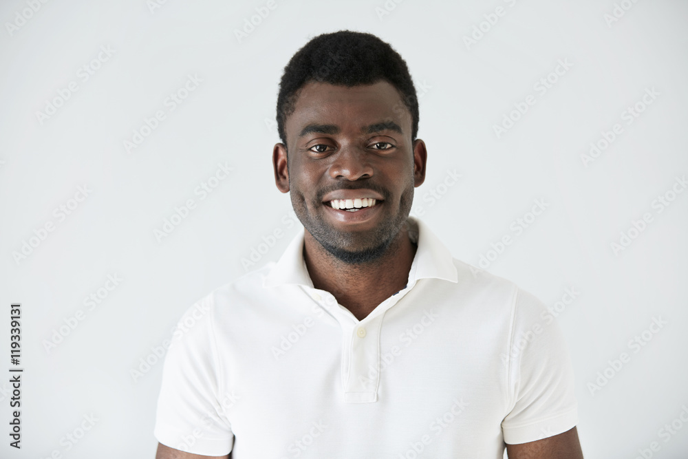 Cropped shot of smiling handsome young casually dressed African man model in white polo shirt, smiling showing his teeth, against studio background with copy space for your promotional information Cropped shot of smiling handsome young casually dressed African man model in white polo shirt, smiling showing his teeth, against studio background with copy space for your promotional information