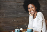 Human emotions and feelings. Young attractive and charismatic dark-skinned woman with curly hair, wearing casual clothes, drinking coffee with cake posing with big smile showing her teeth in braces