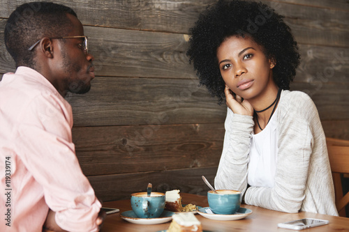 Two young black smart managers discussing very important question sitting at coffee shop  searching for new brilliant idea for developing strategy of successful business  woman having thoughtful look