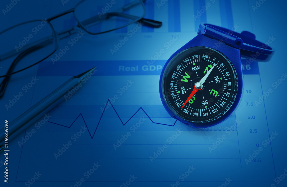 Blue compass with pen and glasses on growth financial chart and