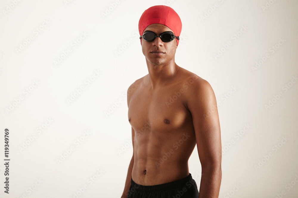 A portrait of a fit attractive olympic swimmer wearing red cap and black goggles looking straight at the camera against white background