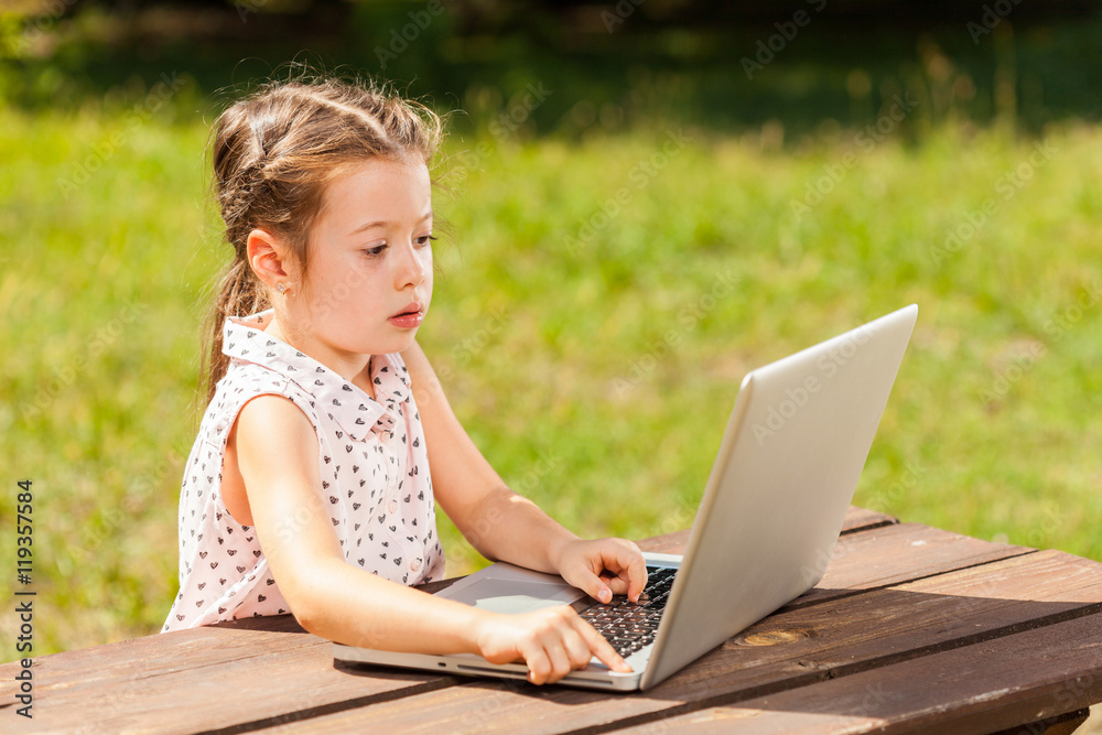 Smiling brother and sister sitting on table in park and using laptop Smiling brother and sister sitting on table in park and using laptop