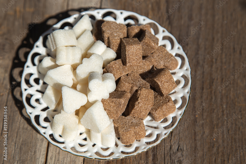 There is a figured brown and white sugar on a porcelain white saucer.There is a saucer on the wooden surface. There is a figured brown and white sugar on a porcelain white saucer.There is a saucer on the wooden surface.