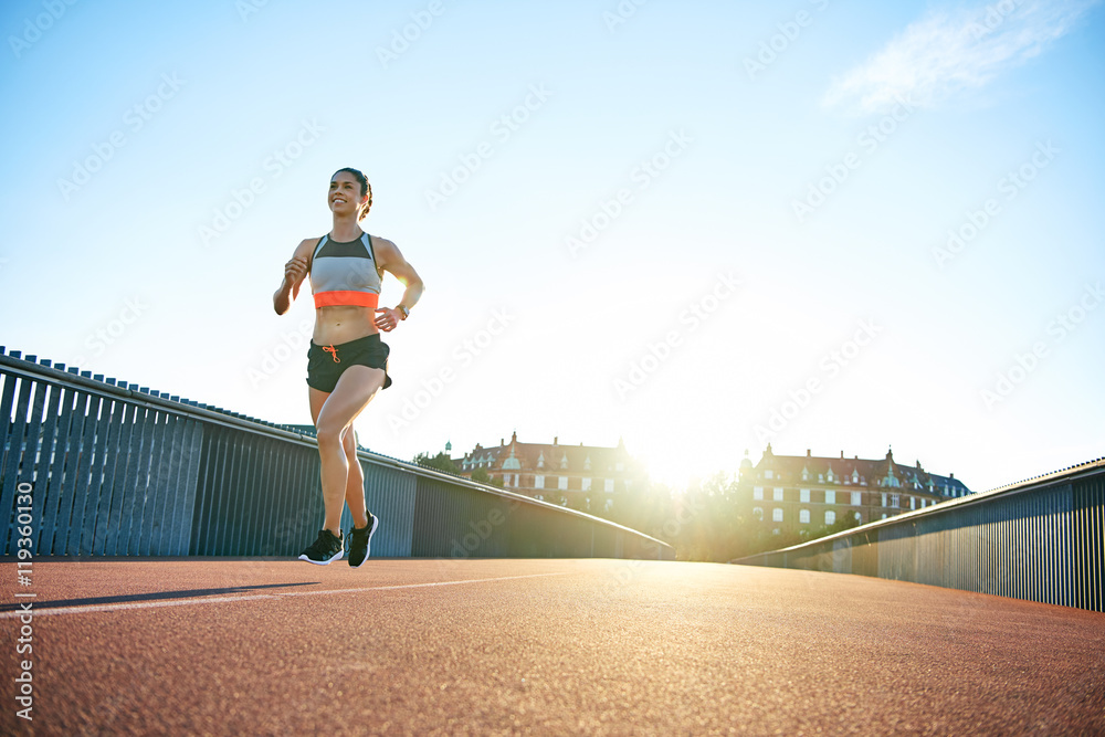Low angle of sun behind woman running along bridge Low angle of sun behind woman running along bridge