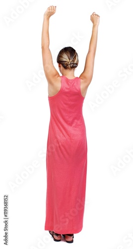 back view of dancing young beautiful woman. girl watching. A slender woman in a long red is raising his arms up.