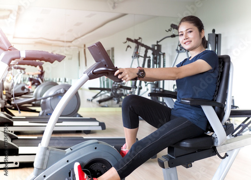 Asian woman riding stationary bike in gym.