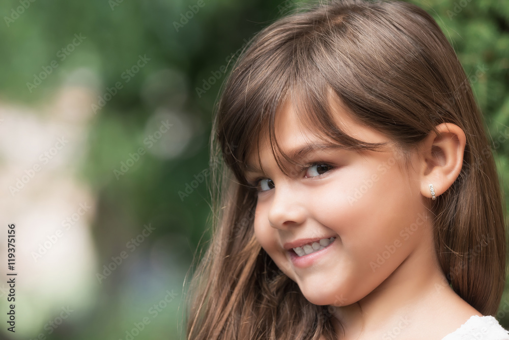 Portrait of smiling attractive little girl outdoors. Little girl peeks at the camera