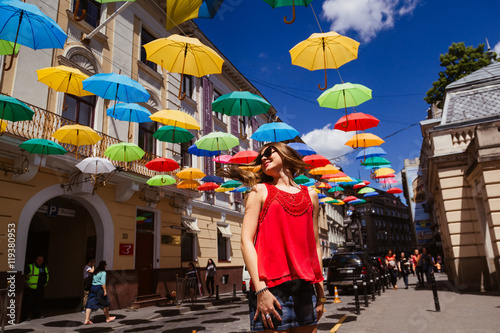 Girl in foxy sunglasses whirls under colorful umbrellas