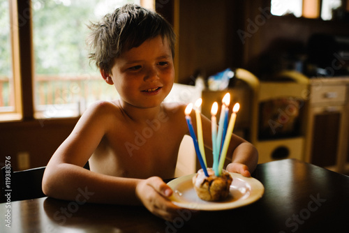 Young boy holding a cupcake with candles and smiling