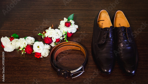 Black leather shoes, belt and boutonniere lie on the floor