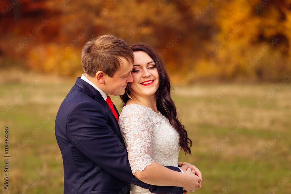 Handsome groom in blue jacket and red tie hugs bride from behind Handsome groom in blue jacket and red tie hugs bride from behind