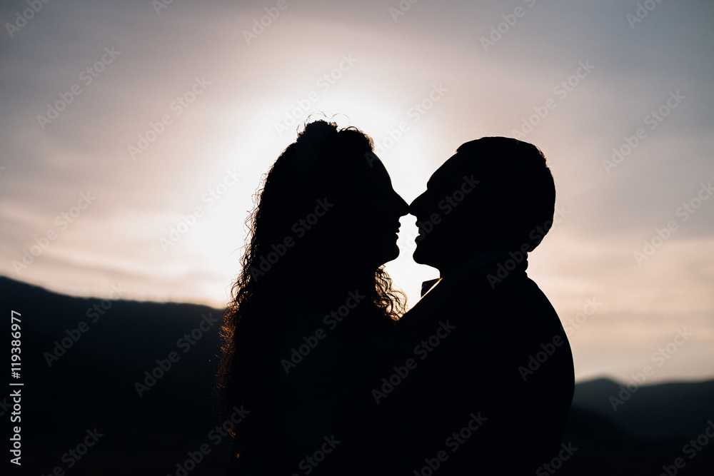Silhouettes of couple standing on the hill and kissing in the li