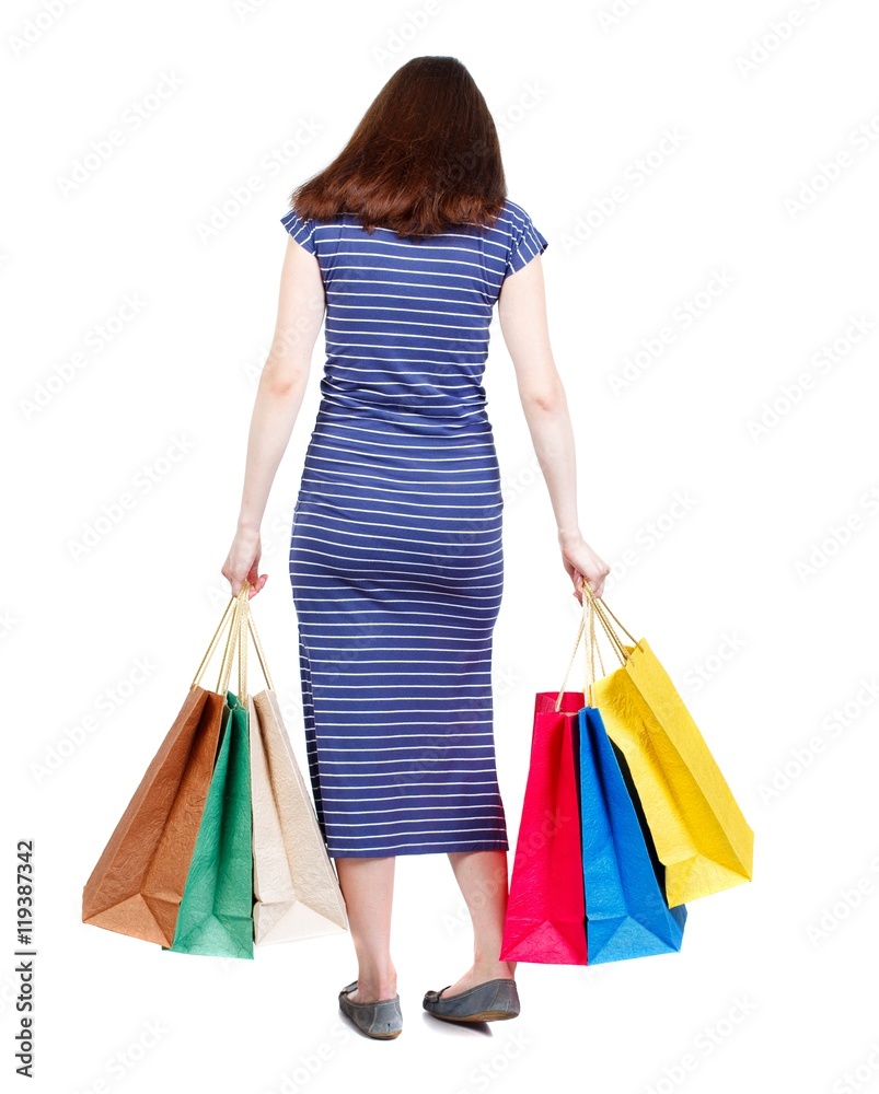 back view of woman with shopping bags. brunette in a blue striped dress standing with shopping bags and looking down.