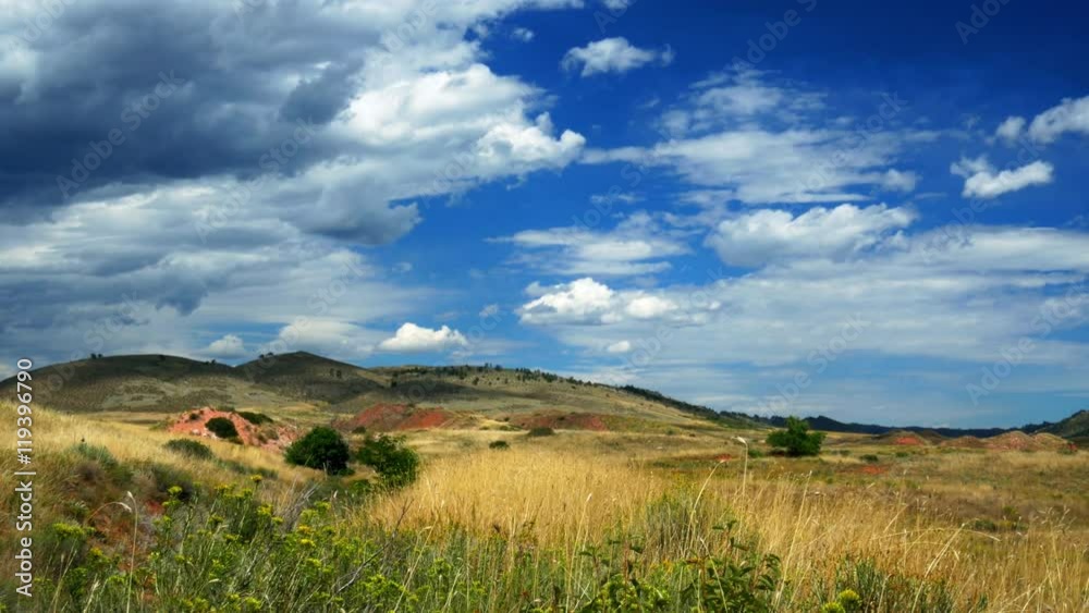 A light breeze gently moves wild grasses and white fluffy clouds in this picturesque scene of rolling hills not far from the city of Loveland Colorado A light breeze gently moves wild grasses and white fluffy clouds in this picturesque scene of rolling hills not far from the city of Loveland Colorado