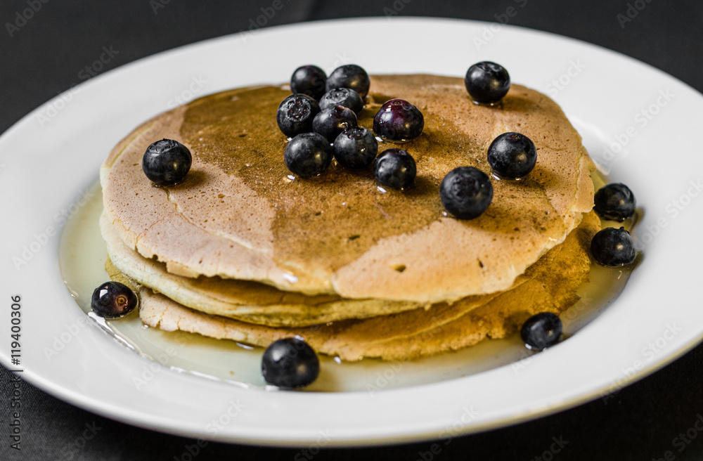 Close up of a tasty american pancake with blueberries and maple syrup. Selective focus.