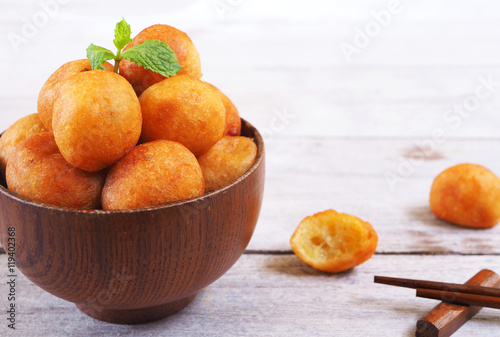 Close up of a bowl of deep fried sweet potato balls on a wooden table.