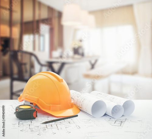 architectural blueprint with safety helmet and tools over luxury dining room interior.