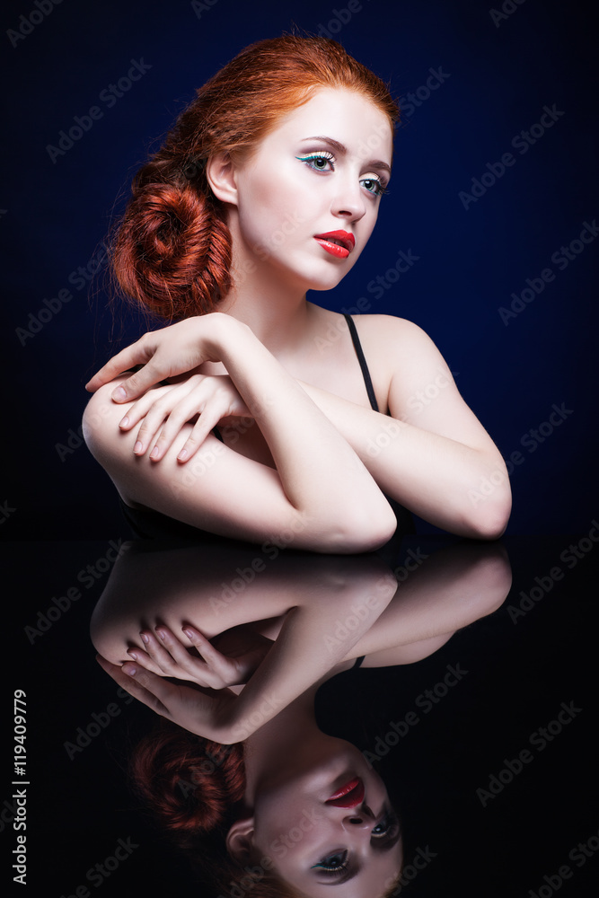 Naklejka premium Young woman with ginger hair over reflection mirror on blue back