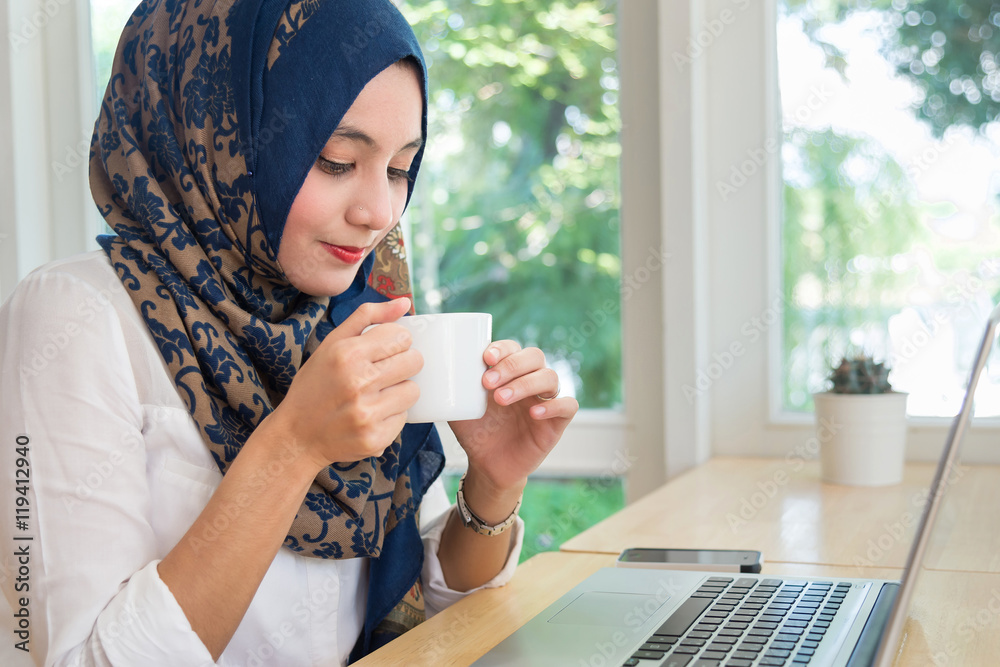 Muslim woman with computer on table , holding a coffee cup. Muslim woman with computer on table , holding a coffee cup.