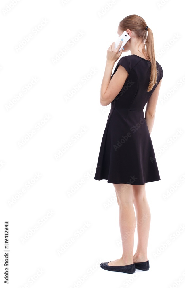 back view of a woman talking on the phone. Isolated over white background. Blonde in a short black dress talking on the white smartphone. back view of a woman talking on the phone. Isolated over white background. Blonde in a short black dress talking on the white smartphone.