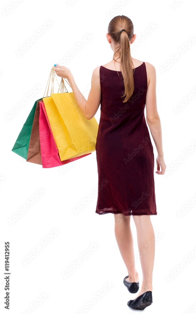 back view of going woman with shopping bags Isolated over white background. The girl in the maroon sleeveless dress holding shopping bags.