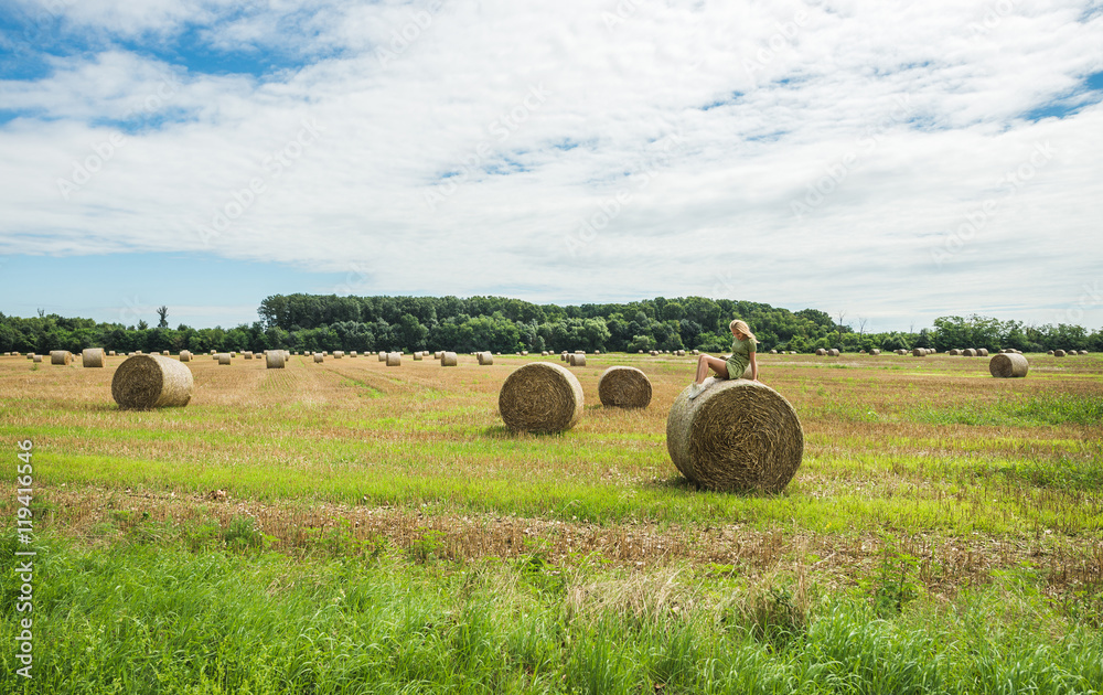Young blond lady sitting on haystack on sunny summer day, Badasconytomaj, Hungary