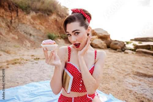Pin up girl with cream cake sitting at the beach