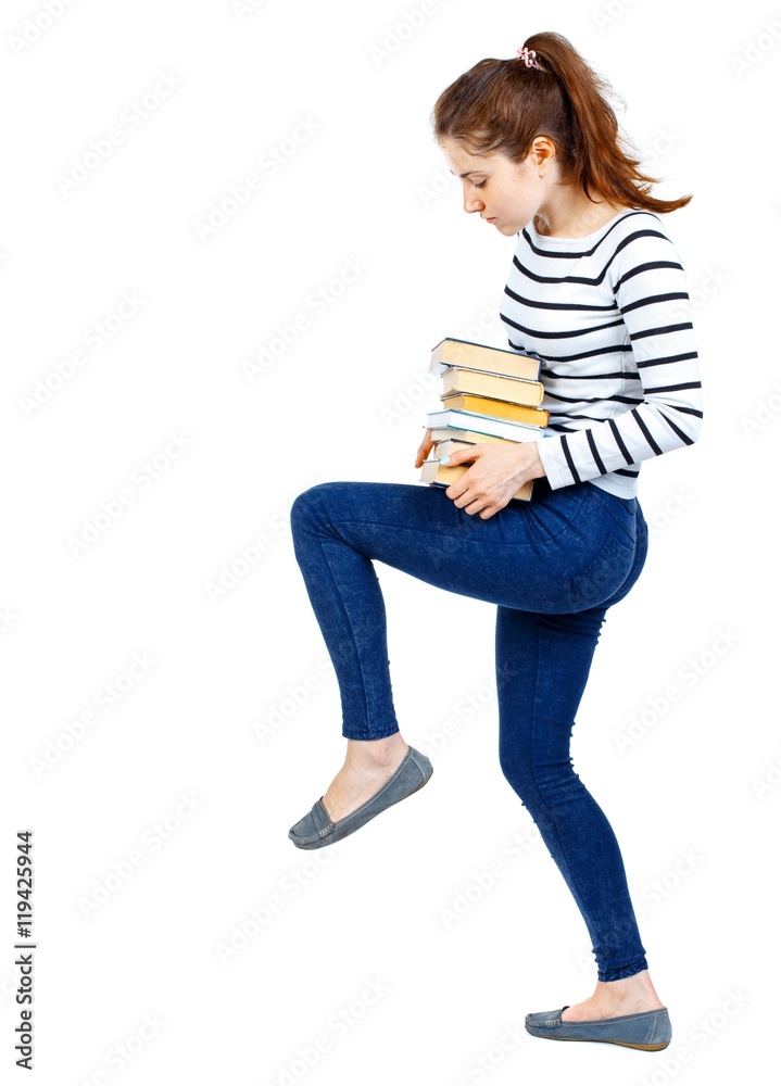Girl carries a heavy pile of books. back view. Rear view people collection. Girl in a striped sweater knee supports books. Girl carries a heavy pile of books. back view. Rear view people collection. Girl in a striped sweater knee supports books.