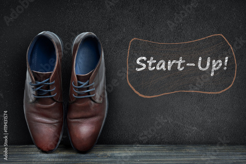 Start-up text on black board and business shoes