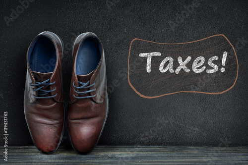 Taxes text on black board and business shoes