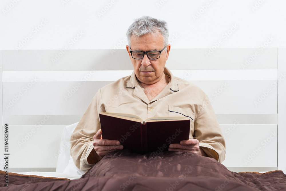 Senior man is lying in bed and reading a book before sleep. Senior man is lying in bed and reading a book before sleep.