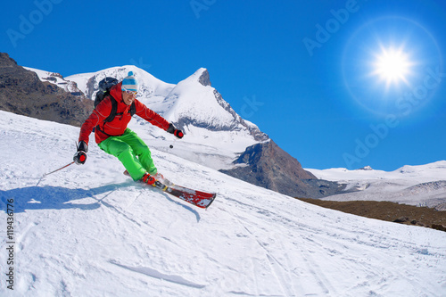 Skier skiing downhill in high mountains against sunshine