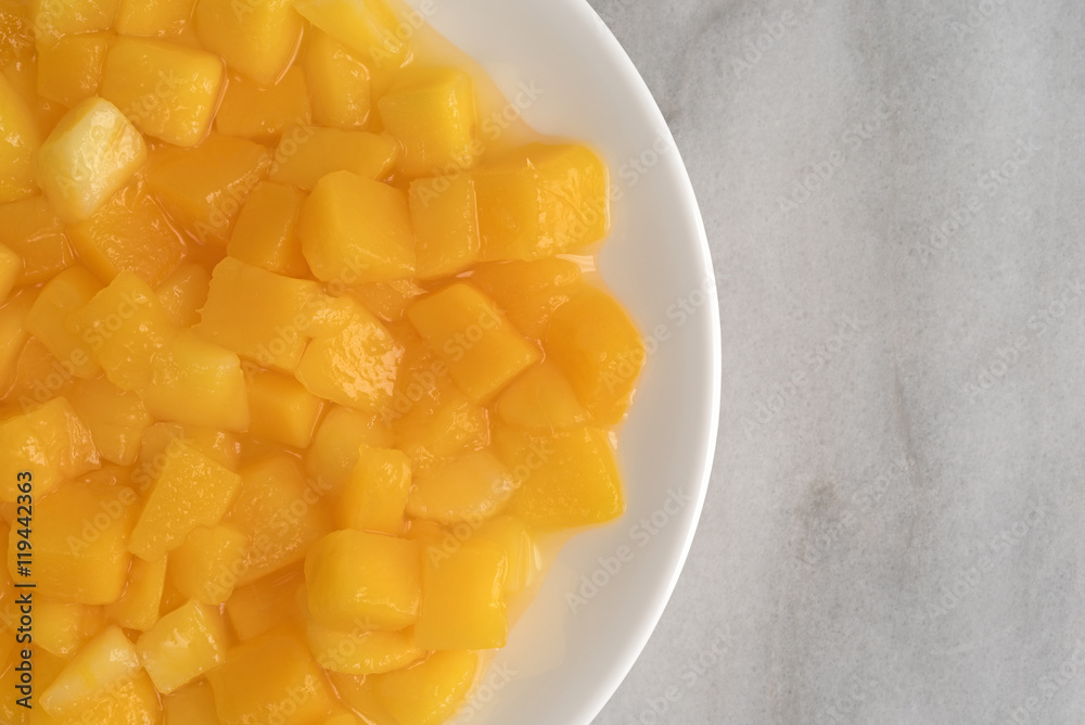 Diced mangoes on a white plate atop a marble counter top.