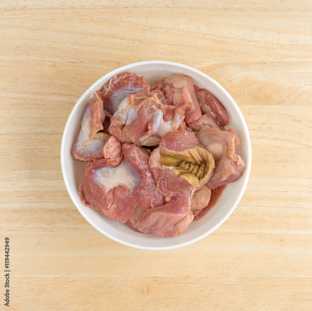 Bowl of fresh chicken gizzards and hearts on a wood table top. Bowl of fresh chicken gizzards and hearts on a wood table top.